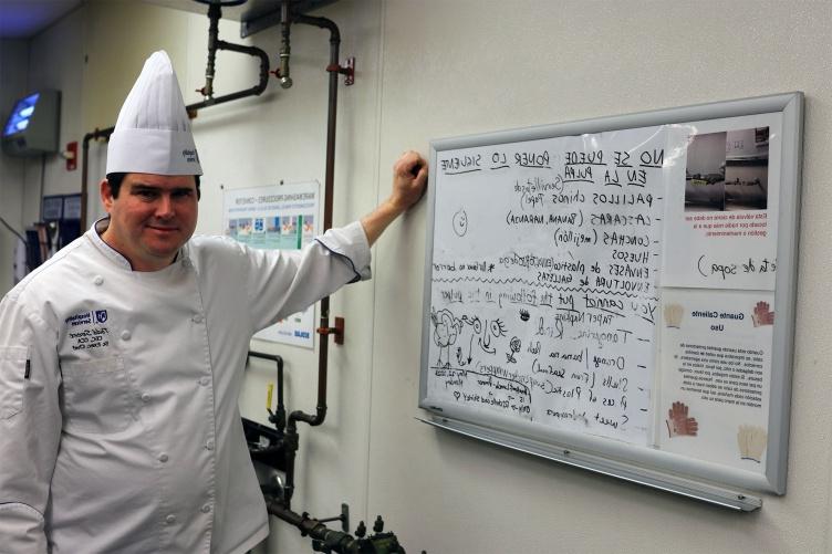 一张照片中，主要研究厨师托德·斯威特(Todd Sweet)穿着厨师装，站在霍洛威公共场所(Holloway Commons)的一块白板旁边，上面写着员工可以将退回的物品堆肥的信息.