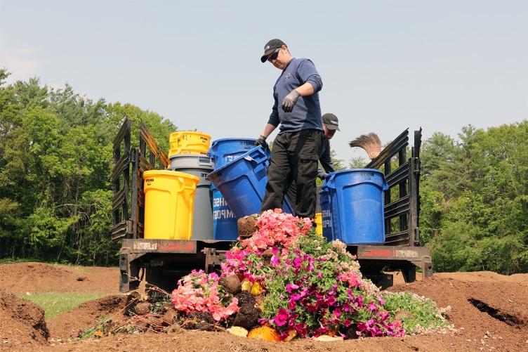 一张主要研究餐饮服务人员在金曼研究农场卸载装满堆肥的桶的照片.