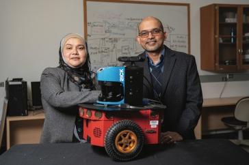 Two researchers st和 in front of a red robot